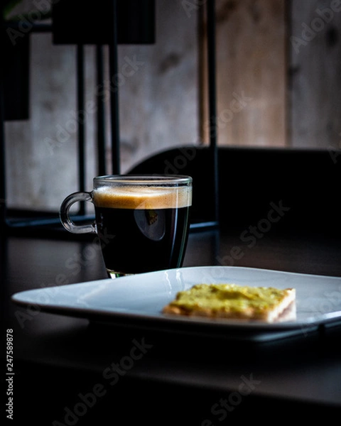 Fototapeta Cup of coffee on a black table with a cracker on a plate for breakfast