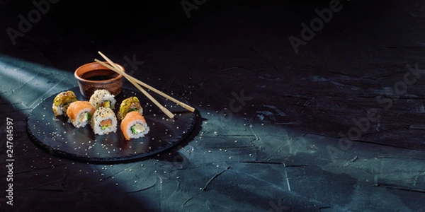 Fototapeta A different assortment of sushi rolls on a black coal board and a dark background. Traditional Japanese cuisine. Food with copy free space for text, logo