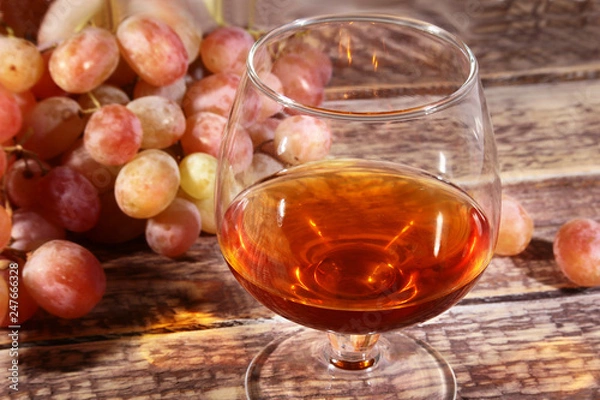 Obraz Glass with Cognac or Brandy and fresh grapes. still life in rustic style, vintage wooden background, selective focus.