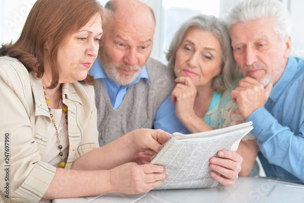 Fototapeta two senior couples sitting at table and reading newspaper