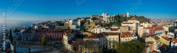 Fototapeta Beautiful panoramic Lisbon landmark with tiny houses with moorish architectural elements on the hill; drone view of picturesque labyrinth of narrow streets and small squares in early morning, Portugal