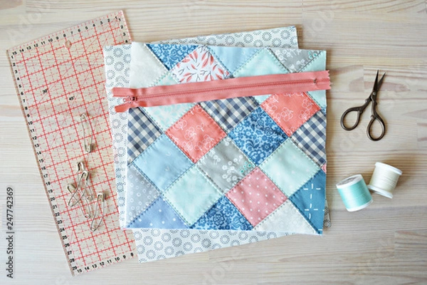 Fototapeta Working process: quilt, zipper, threads, retro scissors	, quilting pins and ruler on the wooden table