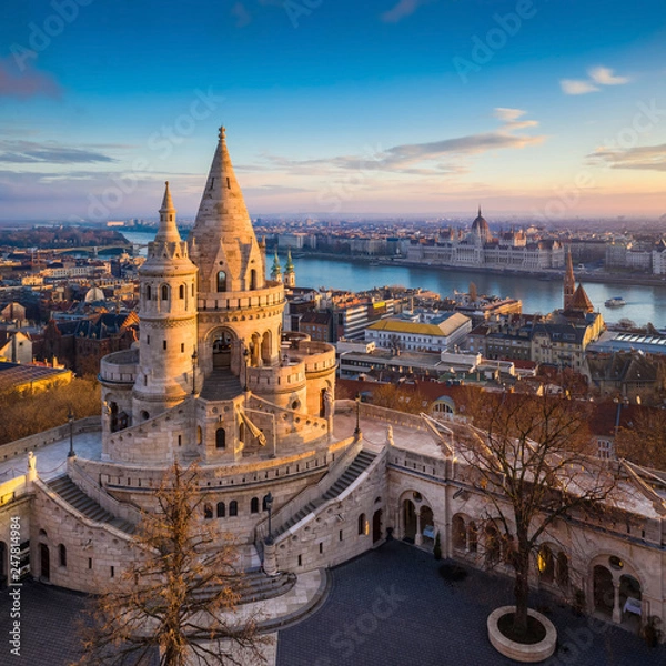 Fototapeta Budapest, Hungary - The main tower of the famous Fisherman's Bastion (Halaszbastya) from above with Parliament building and River Danube at background on a sunny morning