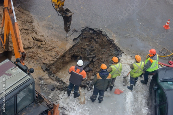 Obraz A group of road workers from public utilities in reflective special vests are discussing an emergency when digging a hole to eliminate the leakage of pipes in the middle of winter