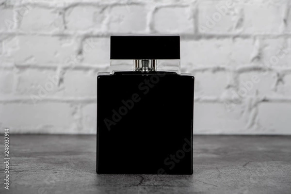 Fototapeta Mock up of a black bottle of men's perfume on a brick gray wall background. Place for text.