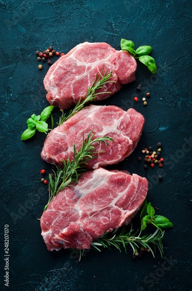 Fototapeta Raw steak. Meat with spices and herbs. On a black stone background. Top view. Free copy space.