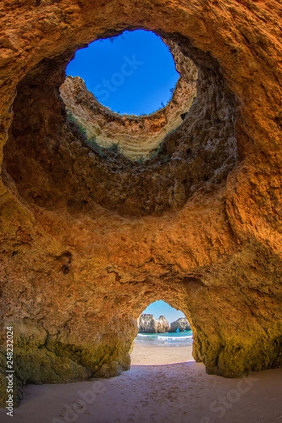 Obraz Famous caves in a beach rock formation in the Algarve, Portugal. Through the one cave you can see the ocean. Through the hole in the ceiling of the cave you can see the blue sky