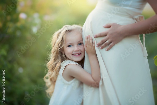 Obraz Happy family: a young beautiful pregnant woman with her little cute daughter walking in the wheat orange field on a sunny summer day. Parents and kids relationship. Nature in the country.
