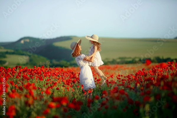 Obraz Mother and daughter in light dresses and hat walking on the farm field. Field of blooming poppies.