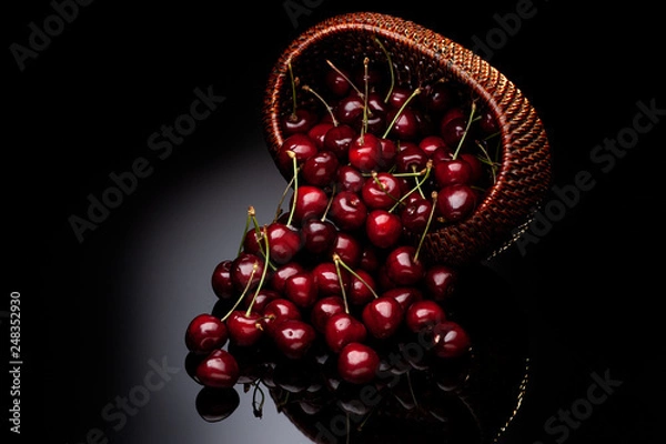 Fototapeta Fresh cherry in a wicker basket on a black background.