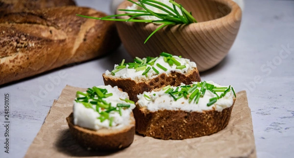 Obraz Pieces of French baguette with fresh green chives, white curd spread placed on rustic paper