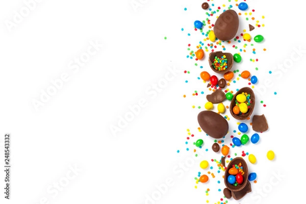 Fototapeta Broken and whole chocolate Easter eggs, multicolored sweets on white background. Concept of celebrating Easter, Easter decorations, search for sweets for Easter Bunny. Flat lay, top view. Copy Space
