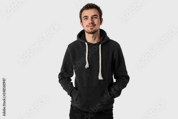 Obraz Portrait of satisfied caucasian young man with hands in his hoodie. Isolated on white background.