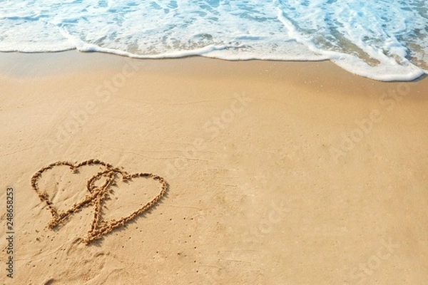 Fototapeta Valentine's day concept, two heart shape drawing on sand beach with wave ocean background.