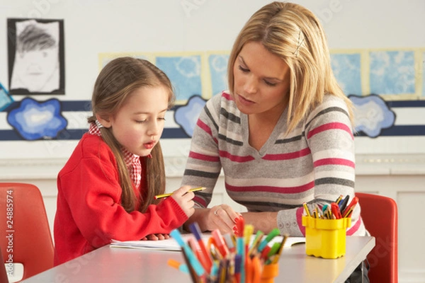 Obraz Female Primary School Pupil And Teacher Working At Desk In Class