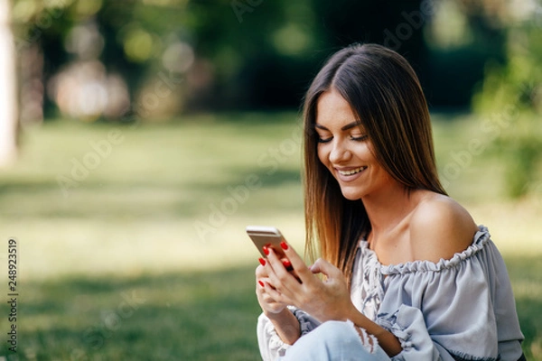 Fototapeta Young woman using a smartphone in the park