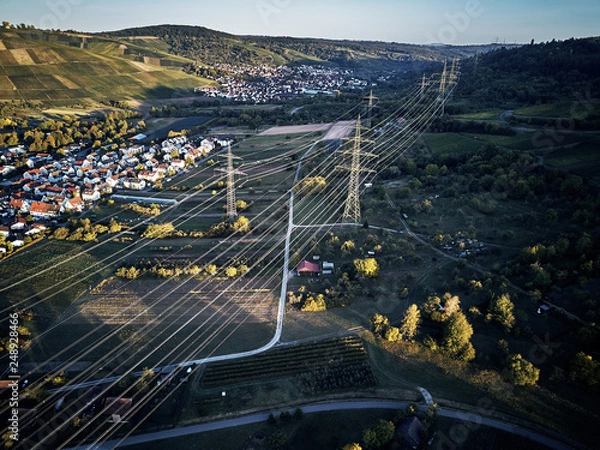 Fototapeta Aerial view of power line pylon near town in the fields on sunset. Orange Teal warm autumn setting