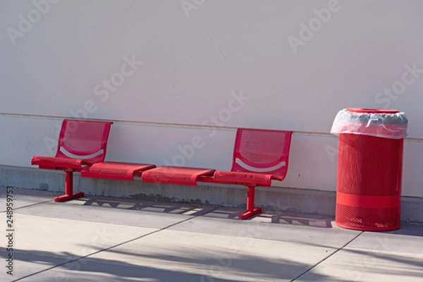 Fototapeta Red metal bench set and garbage can outside a building