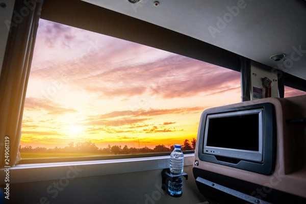 Fototapeta Inside of the bus which has LCD screen blank rear seat for entertainment with a bottle of water and window view of Beautiful landscape nature with sky cloud sunset, Figure tourism road trip concept.