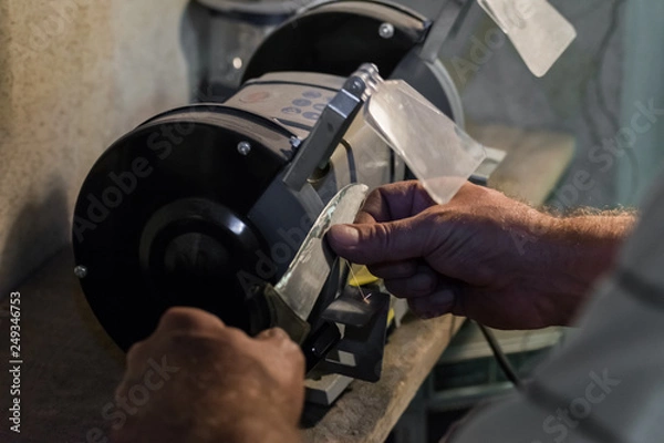 Obraz Man sharpens a knife on an electric grindstone