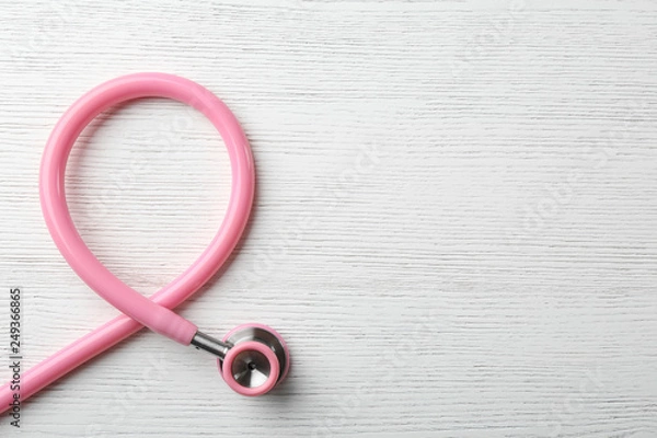 Fototapeta Pink stethoscope folded like awareness ribbon on wooden background, top view with space for text. Breast cancer concept