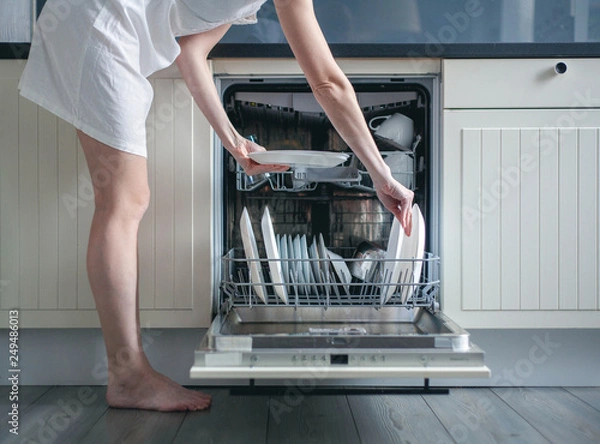 Fototapeta Woman loading dishes into dishwasher, High angle view of utensils in dishwasher at kitchen