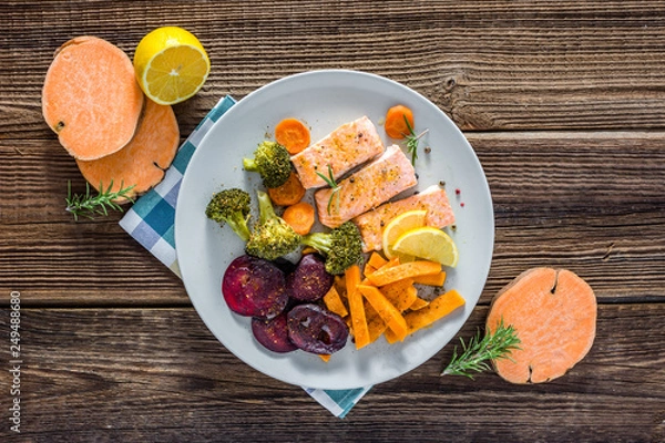 Obraz Baked salmon with vegetables. Cooked fish fillet with fries on plate, top view