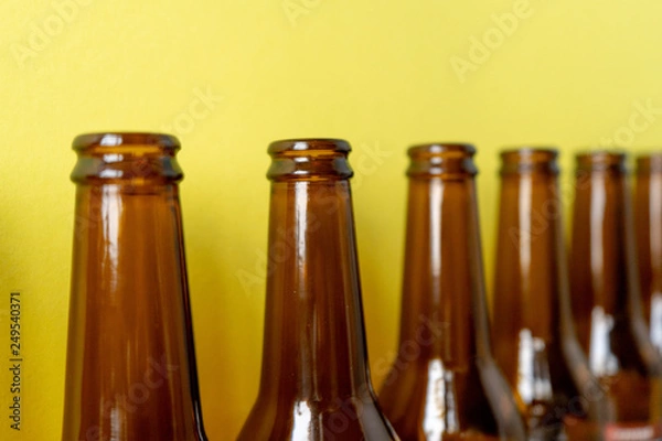 Fototapeta Close-up of empty beer bottles stand in a row diagonally on a yellow background.