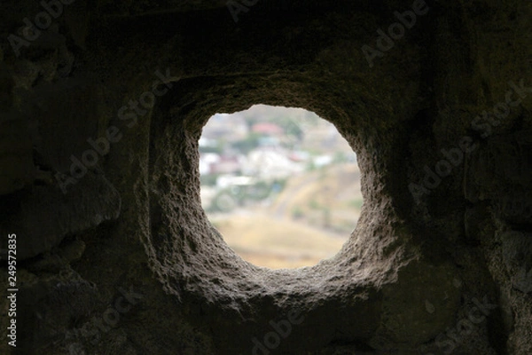 Obraz round uneven hole in dark stone wall with white background. loophole in the fortress wall