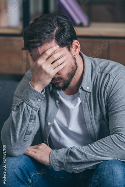 Fototapeta upset man sitting, crying and covering face with hand at home