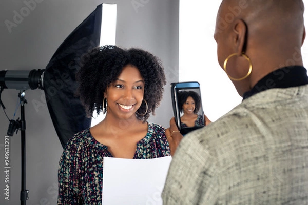 Fototapeta Black female actress doing a self tape audition via cell phone camera in a studio while reading to a casting director.  Depicts the Hollywood entertainment industry process.