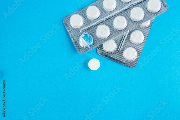 Fototapeta White round pills in pack. Tablets are next to the packaging on a blue background