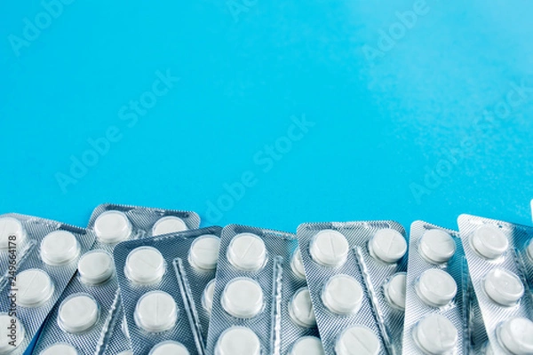 Fototapeta White round pills in pack. Tablets are next to the packaging on a blue background