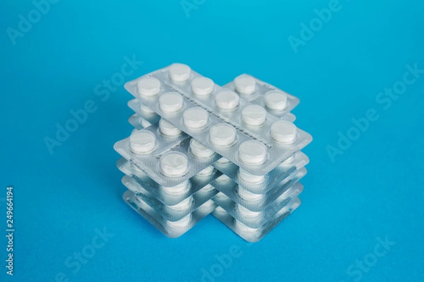 Fototapeta White round pills in pack. Tablets are next to the packaging on a blue background