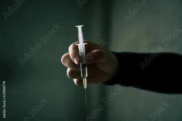 Fototapeta A mysterious hand holding a syringe. Holding the syringe. selected focus.