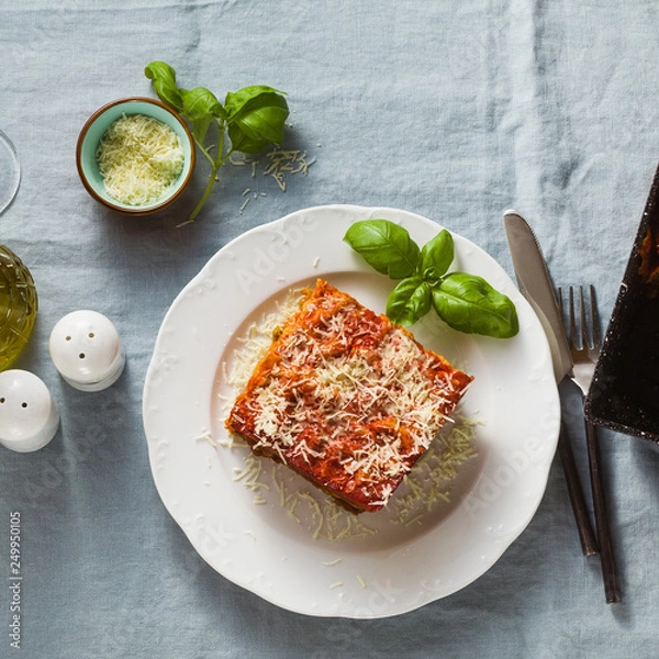Obraz vegan lasagna with lentils and green peas in a baking sheet on a table with a blue linen tablecloth. healthy Italian cuisine for the whole family, party or restaurant and red wine in glasses