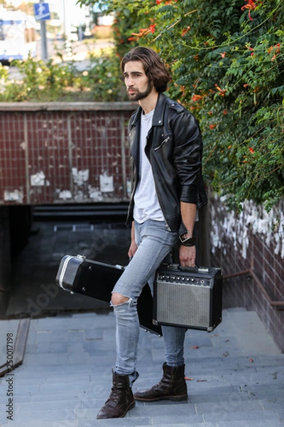 Obraz Street musician holding a case with a guitar and amplifier. Descends into the underground passage. Vagrant lifestyle. Playing to make money a living. Unemployed musician. Future rock star.