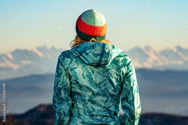 Fototapeta Junge Frau mit Mütze auf die Alpen blickend