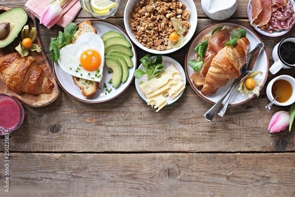 Fototapeta Breakfast food table. Festive brunch set, meal variety with fried egg, croissant sandwich, granola and smoothie. Overhead view