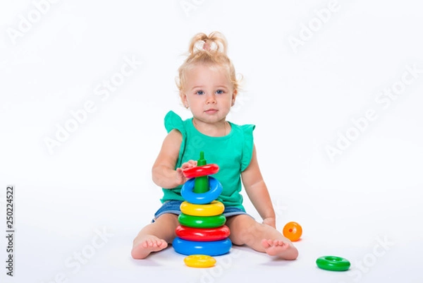 Fototapeta Cute kid blonde girl playing with color pyramid toy isolated on white background. Happy childhood and pre-school development of children