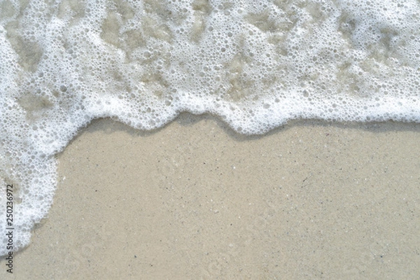Fototapeta Soft wave of the sea on the sandy beach with white clean foam water surf. Top view with copy space.