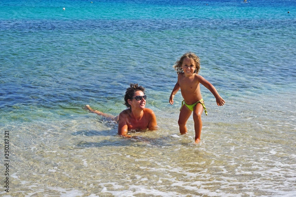 Fototapeta Mother and little daughter play happy in the turquoise sea of Mykonos