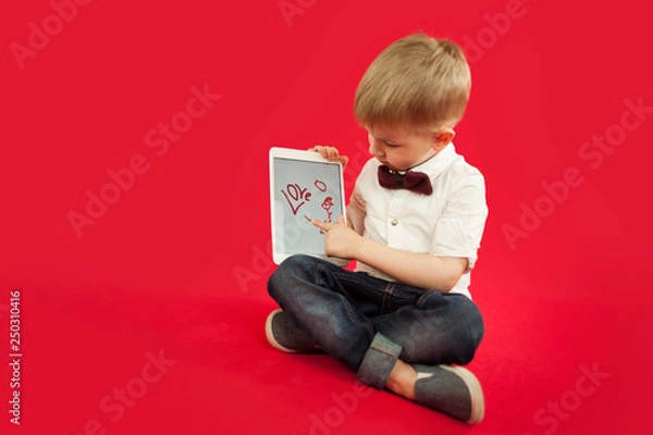 Fototapeta child boy is drawing in tablet ipad red heart on red background. Family and love relationship concept