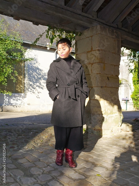 Obraz Femme manteau gris et bottes rouge sous un préau ancien