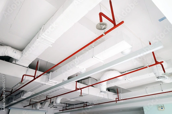 Fototapeta Perspective view of white air duct on the ceiling with red water sprinkler pipe
