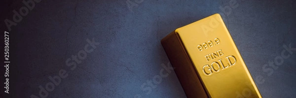 Obraz An ingot of gold metal bullion of pure brilliant diagonally located on a blue textured background.