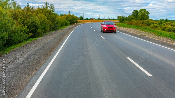 Fototapeta The red car goes on the road. New asphalt highway with fresh road markings