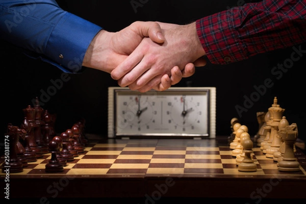 Obraz Handshake of businessmen before a game of chess close-up on a dark background and chess pieces