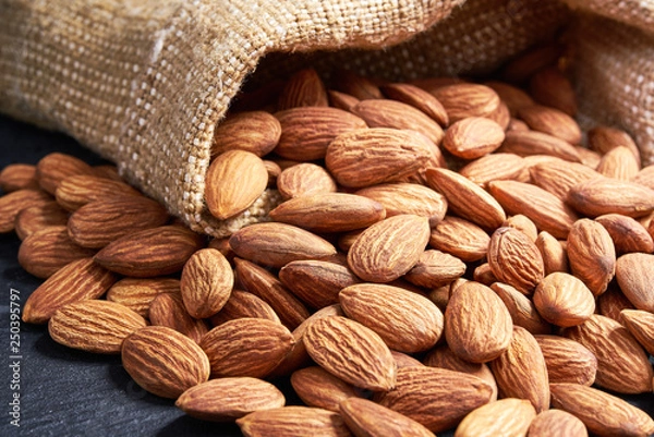Fototapeta Almonds  in burlap sack on black table.
