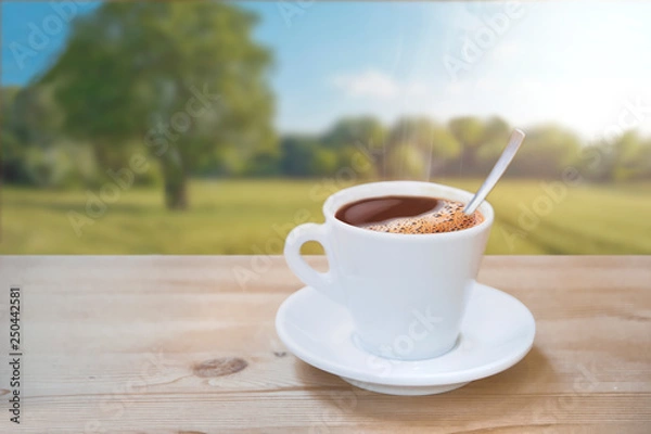 Fototapeta Cup of hot coffee on a natural wooden table against a landscape scene in the nature. Empty copy space for Editor's text.